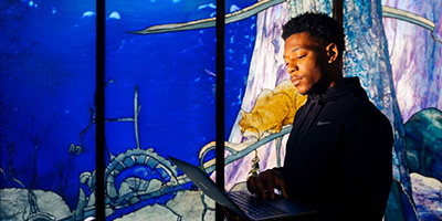 man holding a laptop in front of stained glass windows made to look like an aquarium